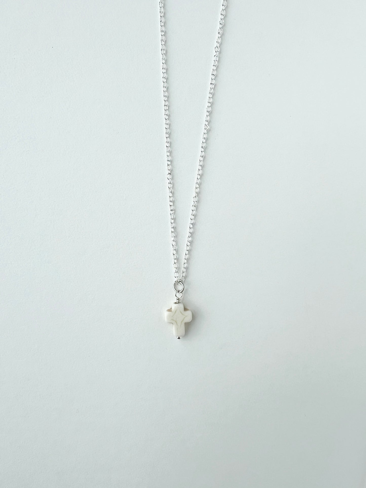 Silver necklace with a small white cross pendant on a white background