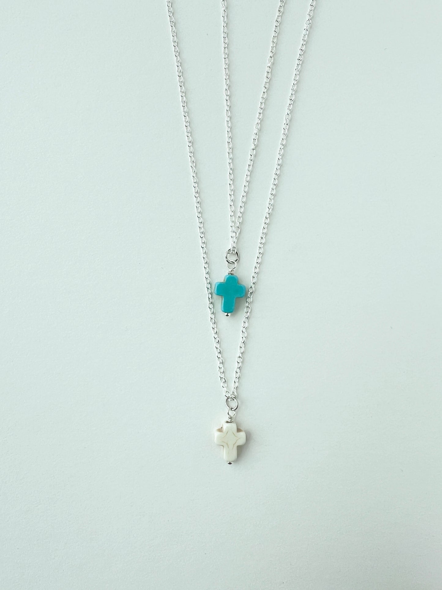 Two silver necklaces with turquoise and white cross pendants on a white background
