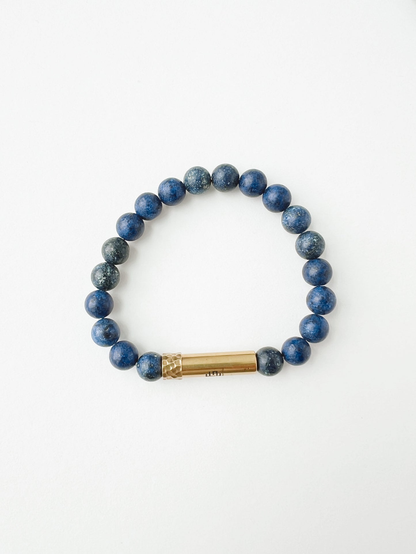 Blue beaded bracelet with a gold cylindrical charm on a white background