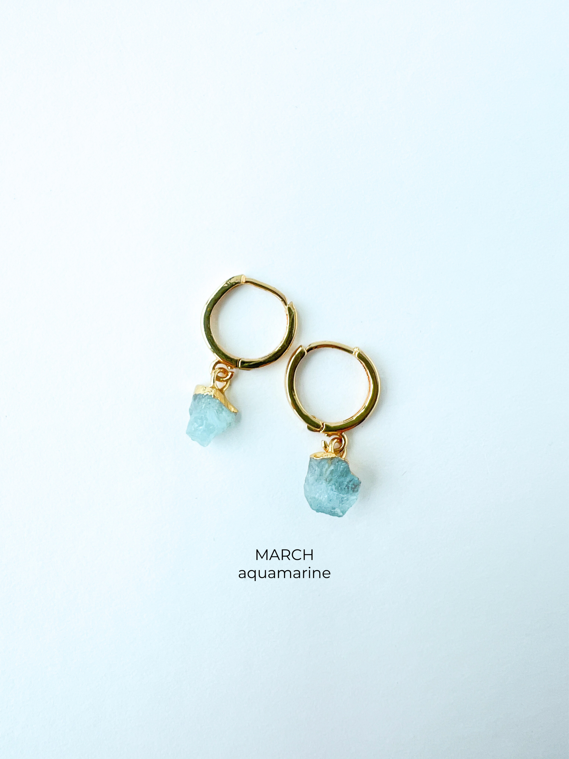 Gold huggie style birthstone earrings in March aquamarine