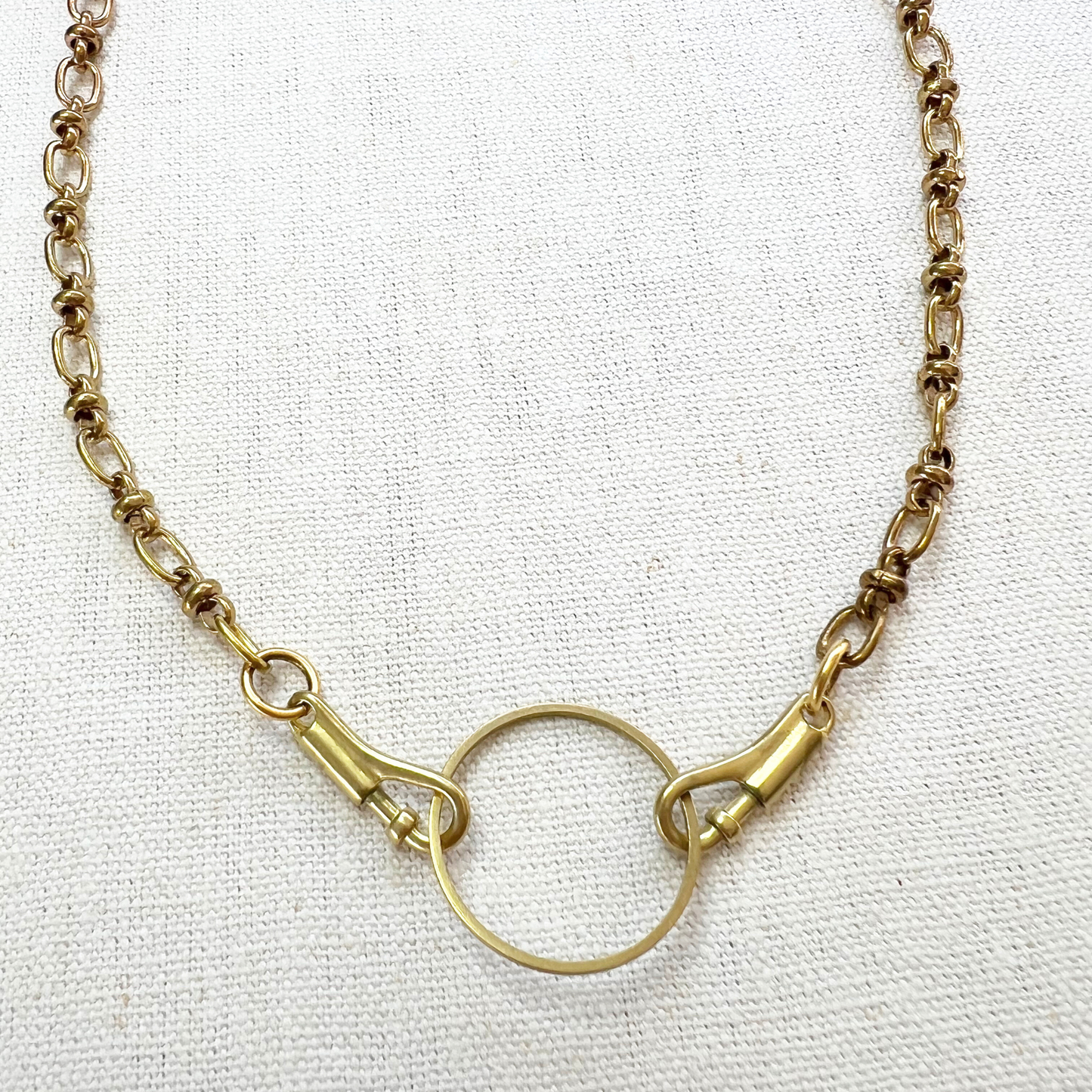 Gold charm necklace with a circular charm holder on a white fabric background