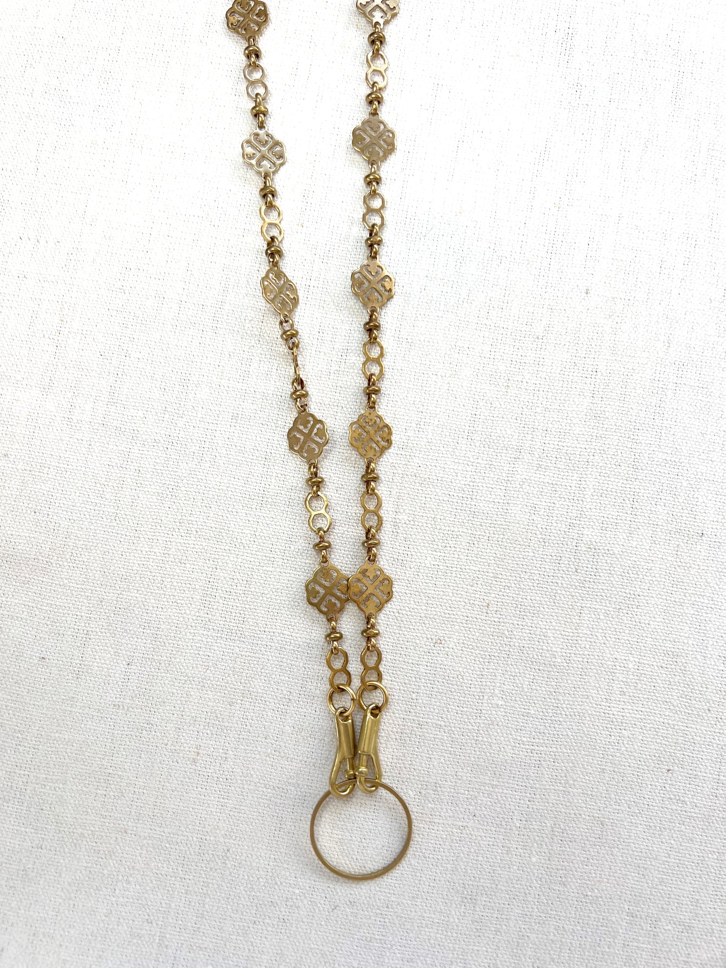 Gold chain necklace with floral designs on a white fabric background