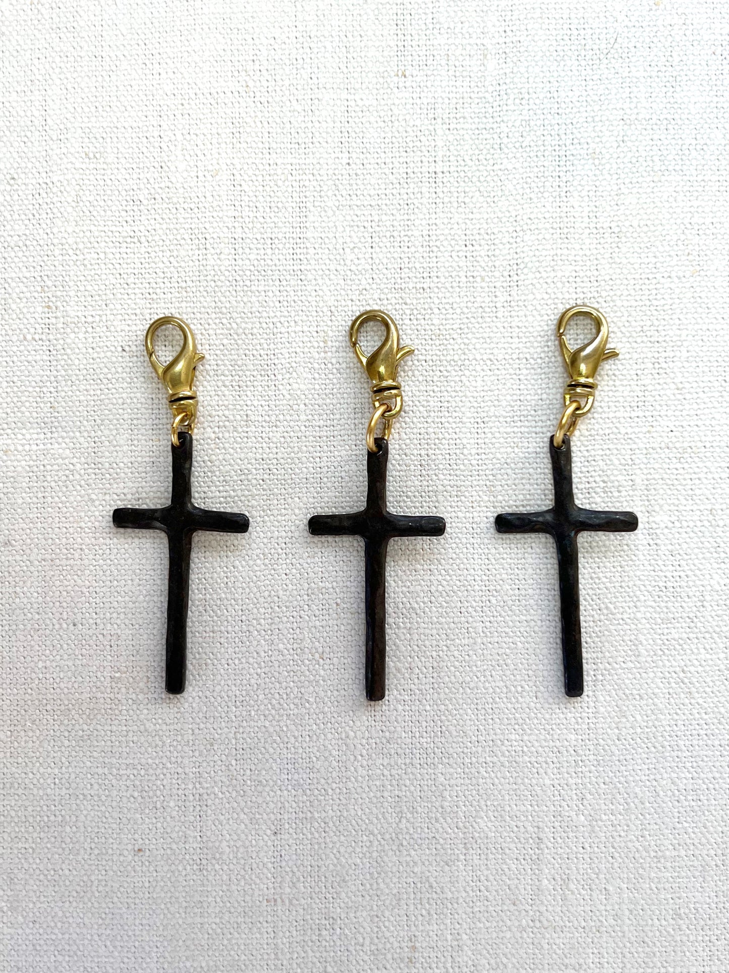Three brown cross-shaped charms with gold loops on a white fabric background
