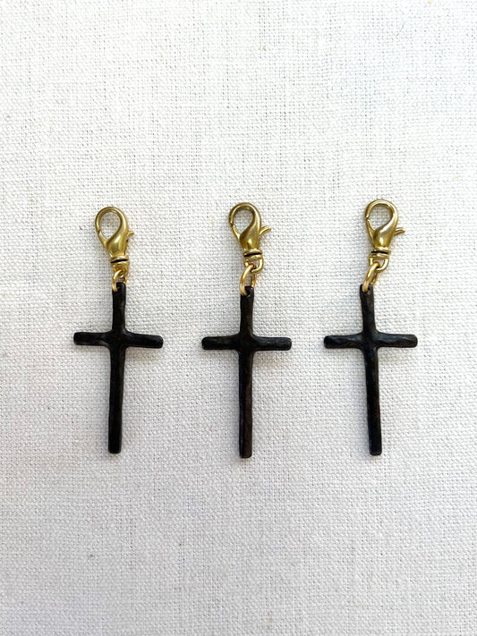 Three brown cross-shaped charms with gold loops on a white fabric background