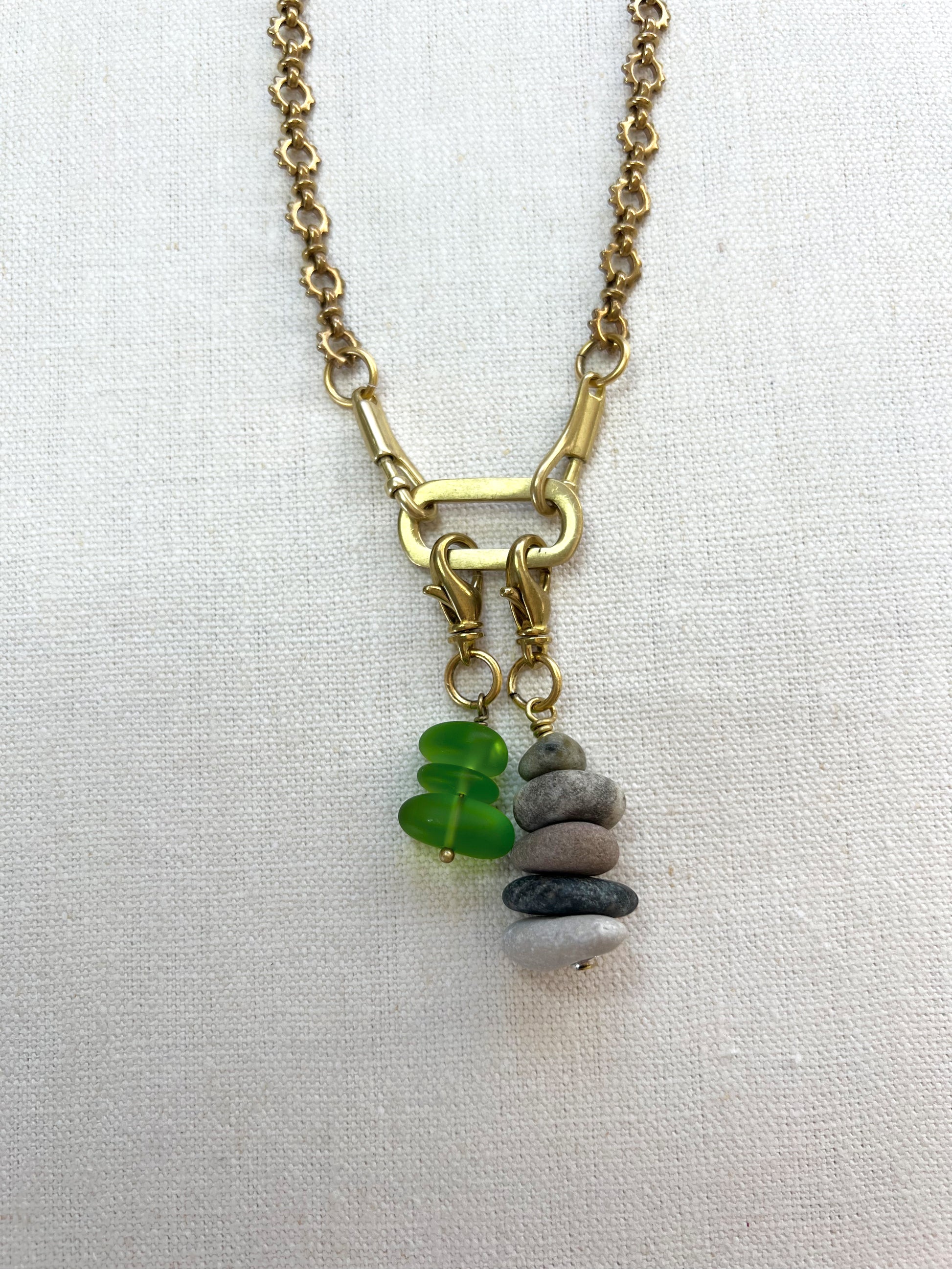 Necklace with a stacked stone cairn charm and green sea glass pendant on a white background