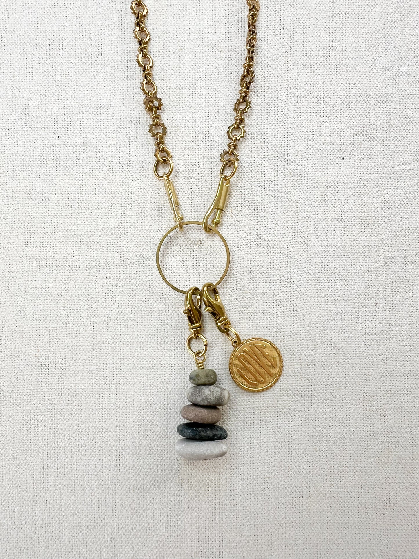 Necklace with pebble charm and gold love charm on a light fabric background