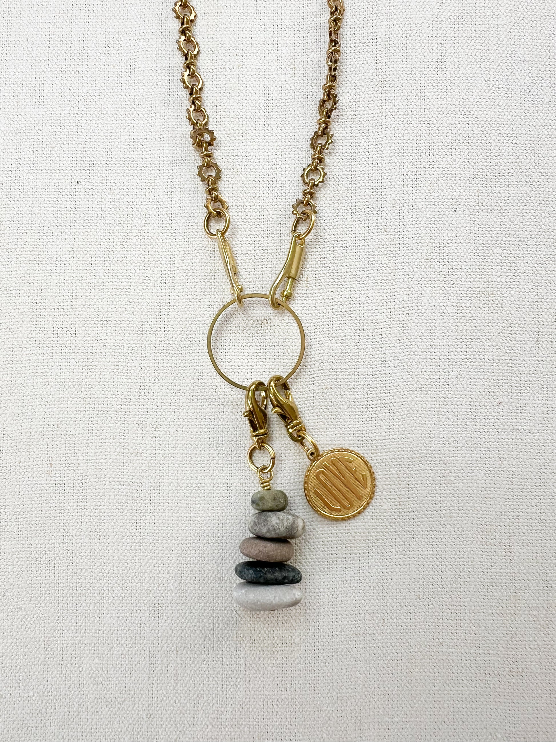 Necklace with pebble charm and gold love charm on a light fabric background