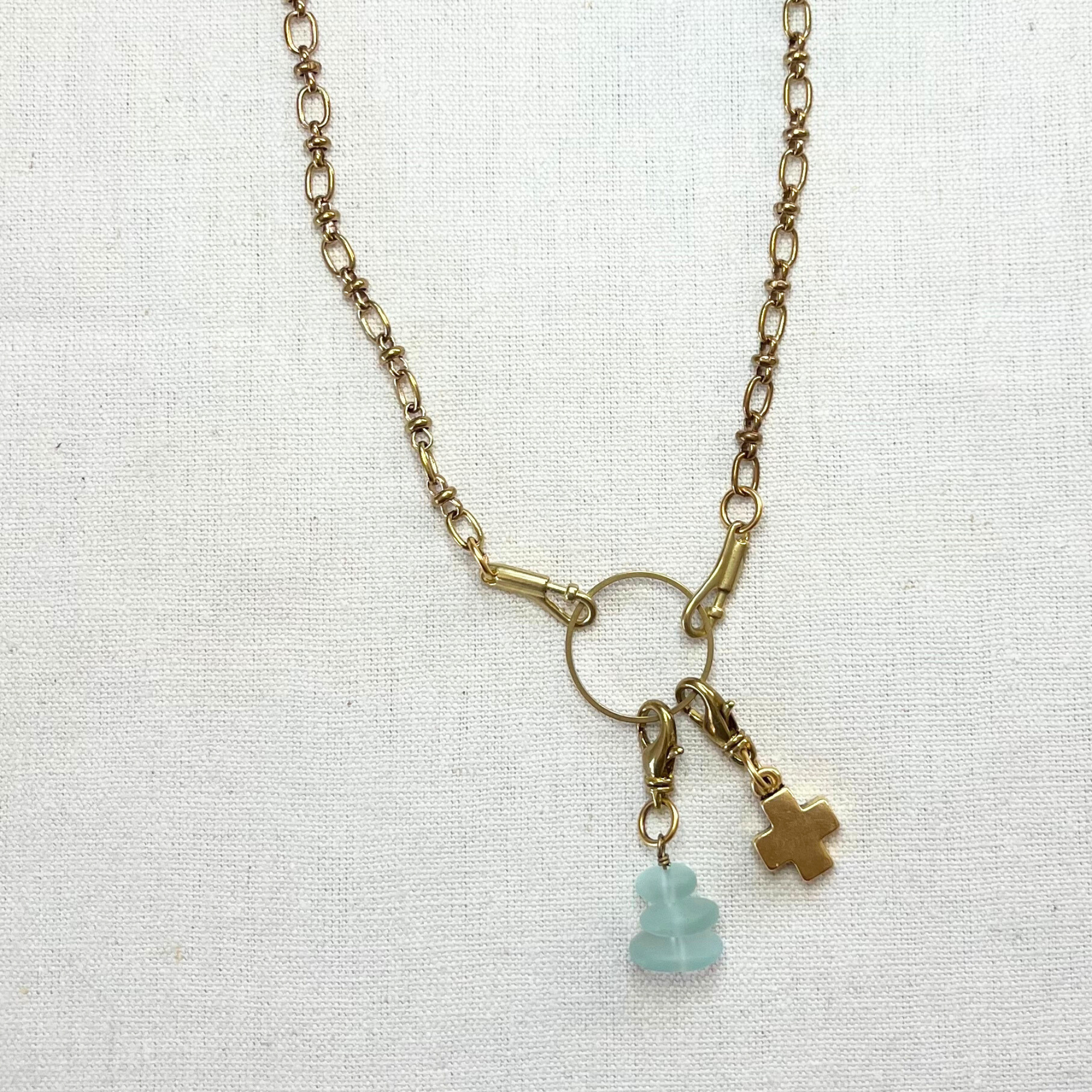A gold charm holder necklace with gold block cross and sea glass charms.