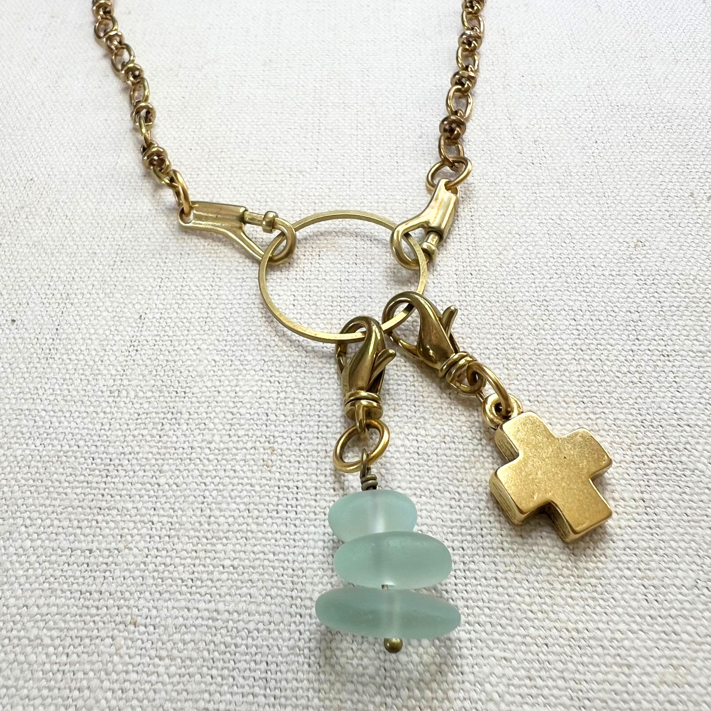 A gold charm holder necklace with gold block cross and sea glass charms.