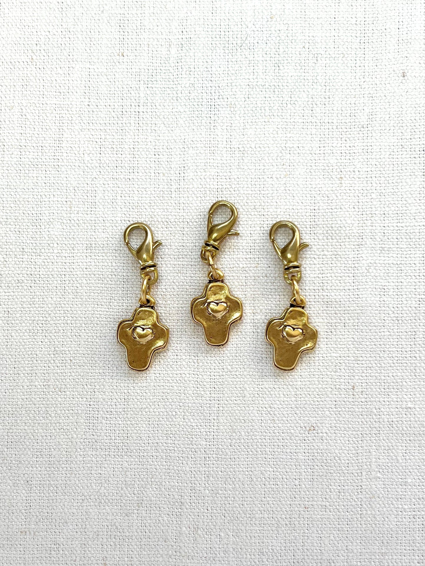 Three gold cross and heart charms on a white fabric background