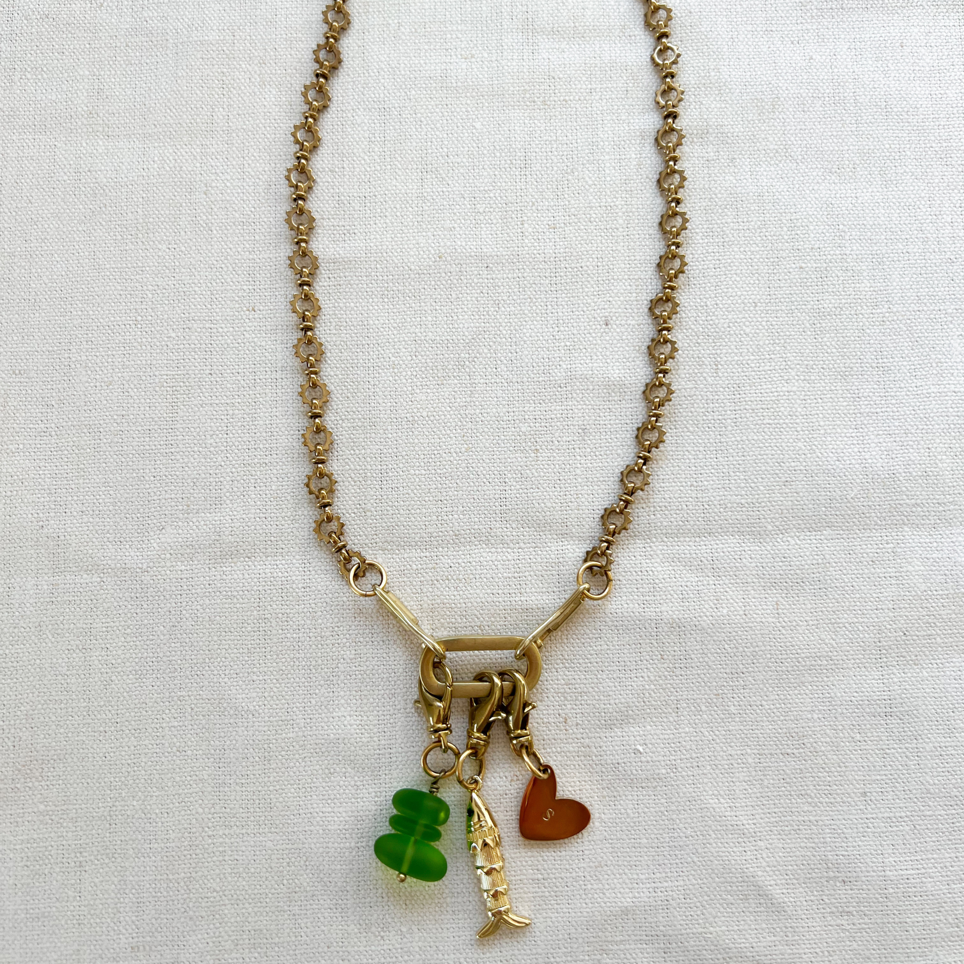 Necklace with sea glass, fish, and heart charms on a white fabric background
