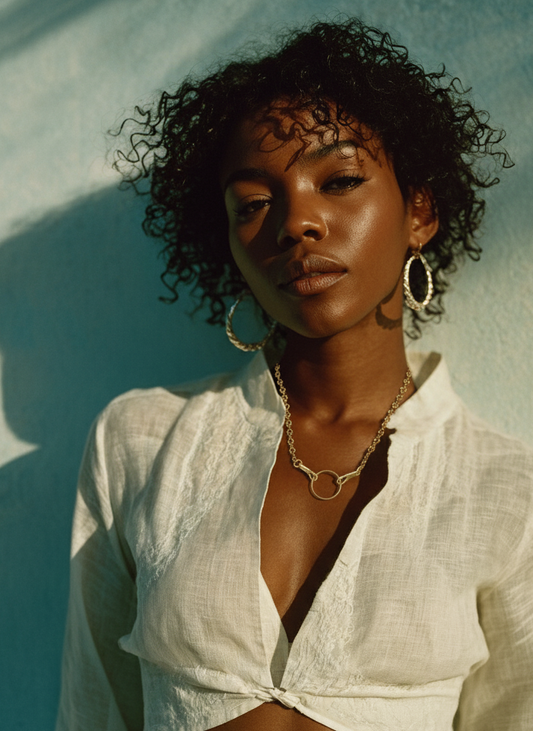 Woman wearing a white outfit against a light blue background with a gold charm necklace.
