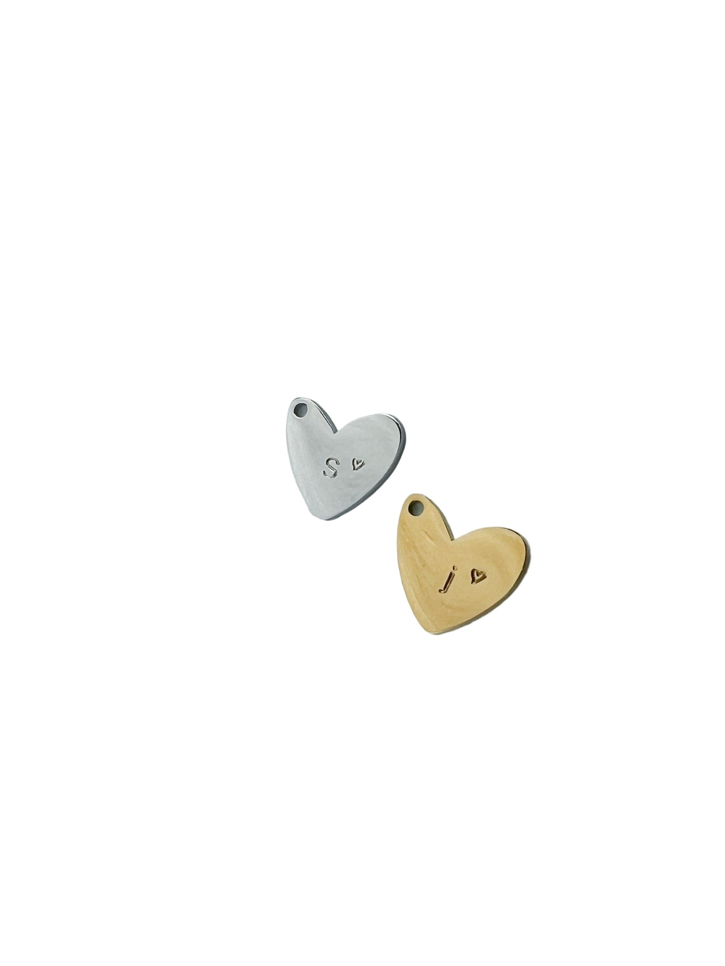 Two heart-shaped pendants, one silver and one gold, on a white background. Handstamped with an initial and a tiny heart.
