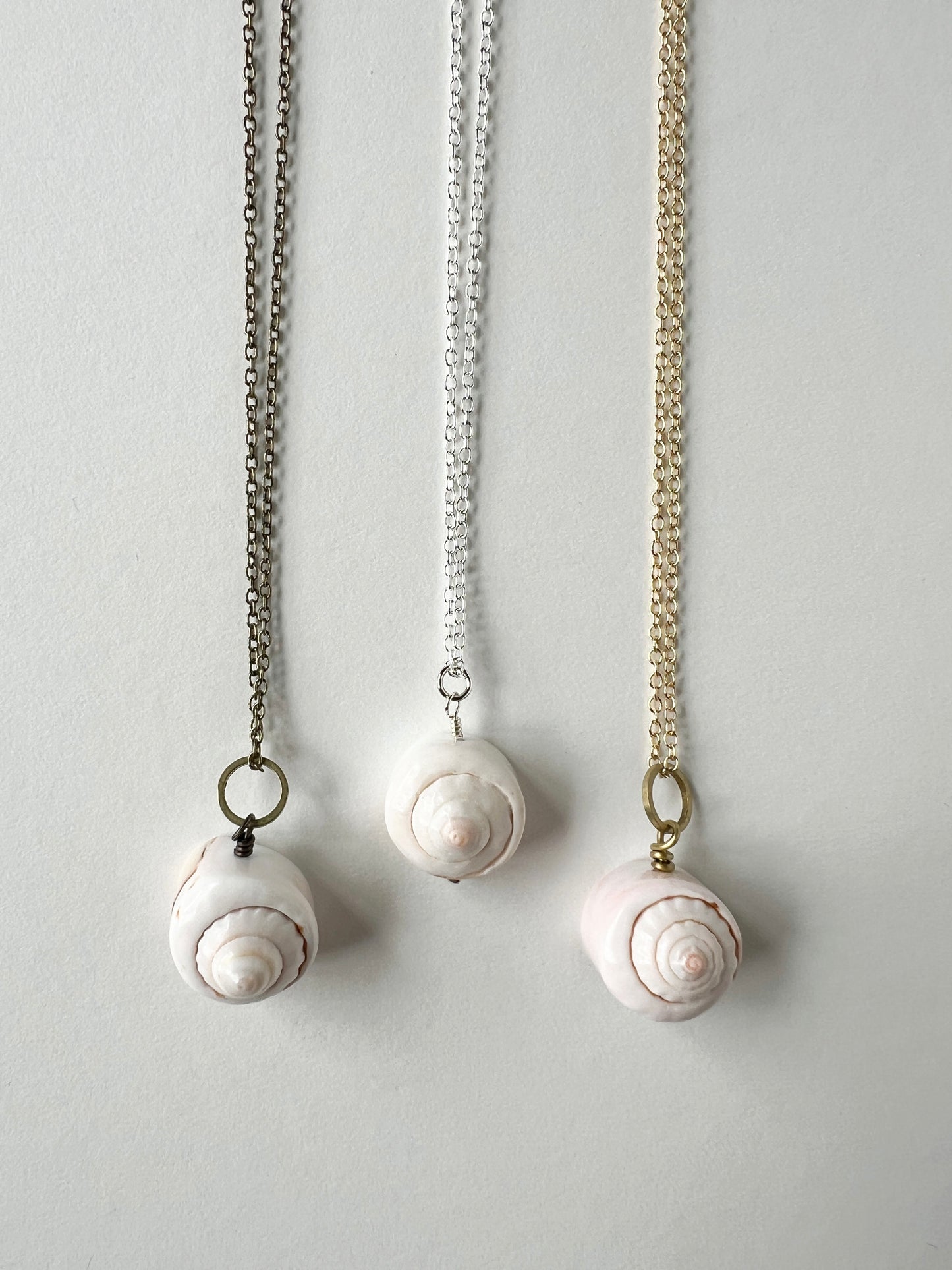 Three shell pendant necklaces on a light gray background