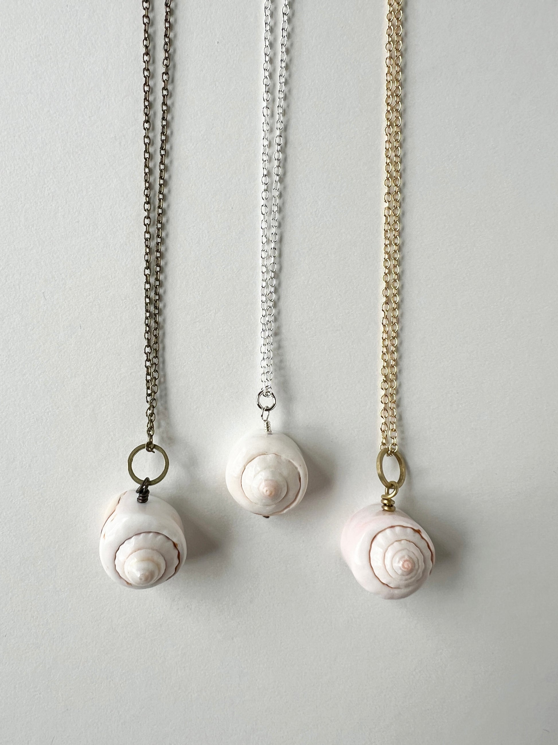 Three shell pendant necklaces on a light gray background