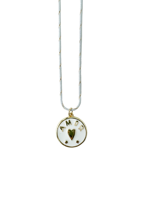 White and gold striped necklace with a circular 18k gold filled pendant featuring a heart and the word Amor on a light gray background