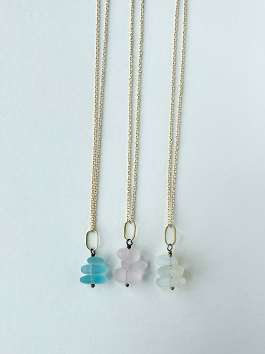 Three gold necklaces with different colored sea glass pendants on a white background
