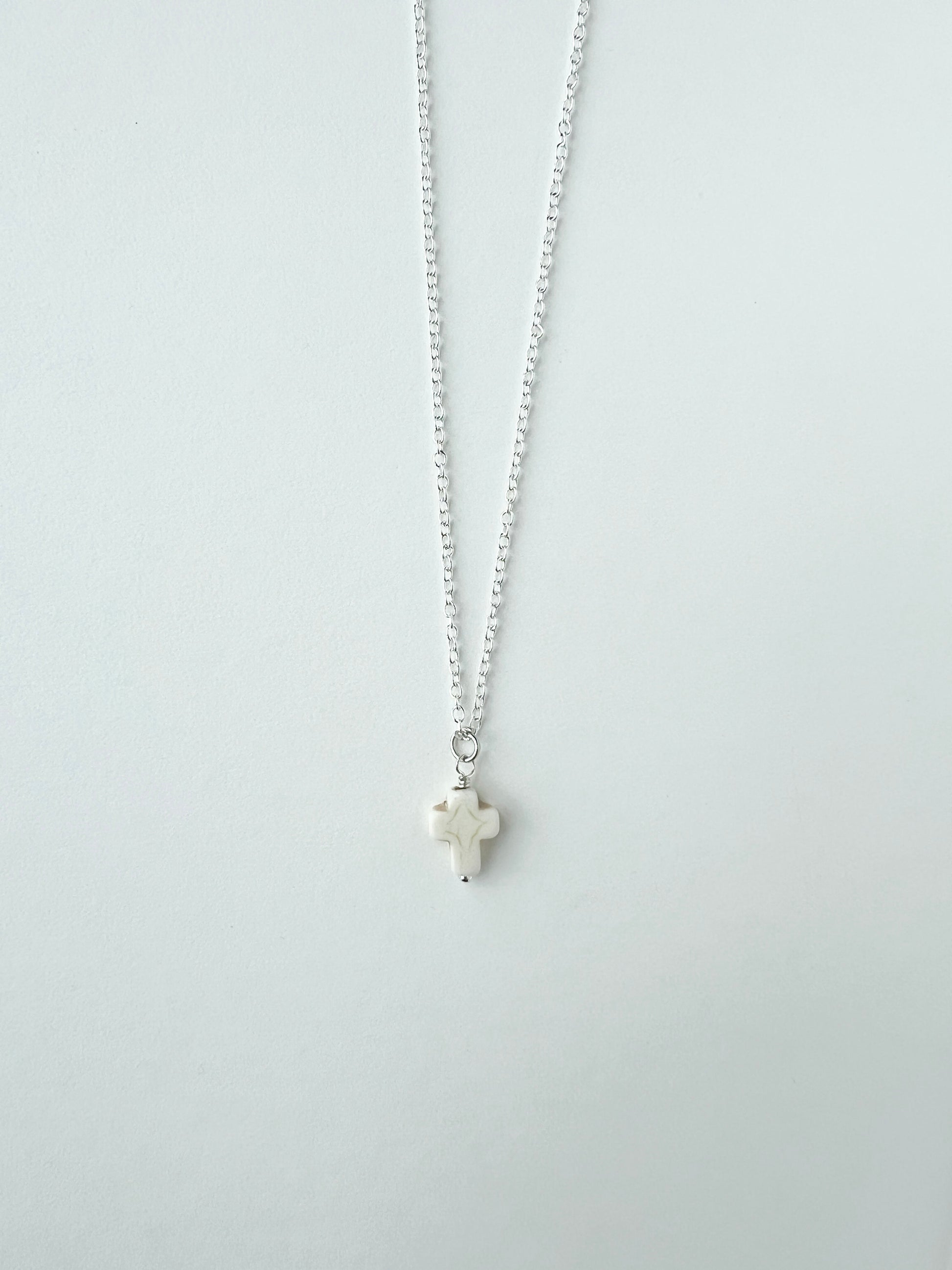 Silver necklace with a small white cross pendant on a white background
