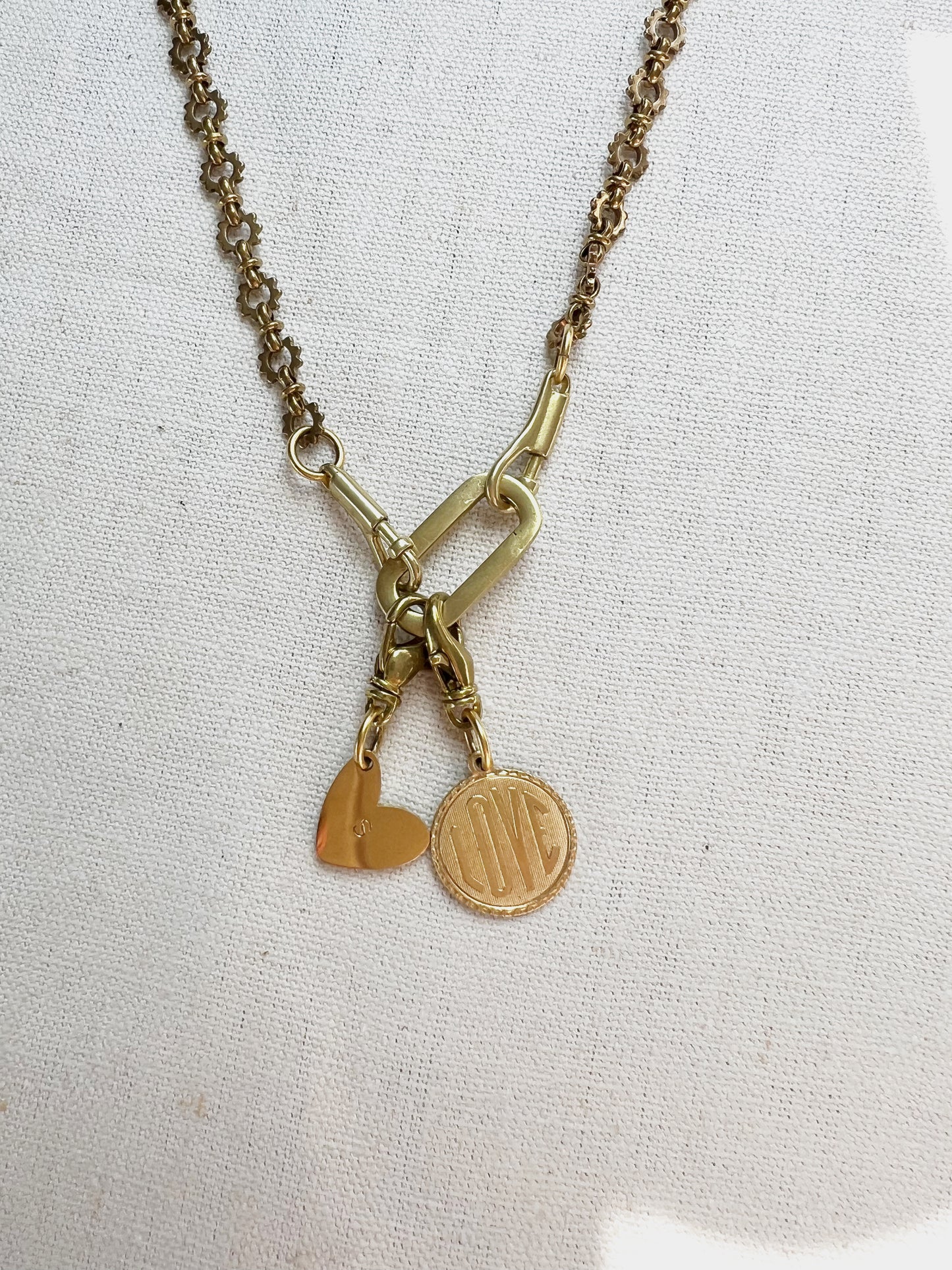 Gold necklace with heart and round pendants on a light fabric background