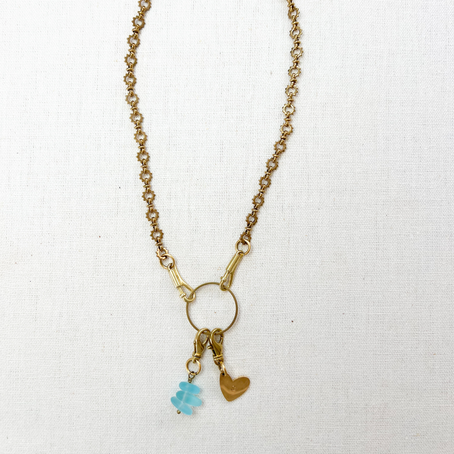 Gold necklace with a blue sea glass charm and heart pendant on a white background