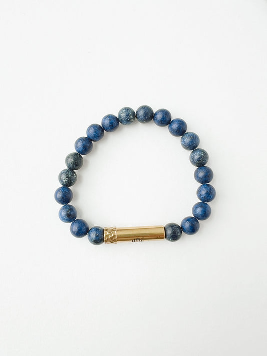 Blue beaded bracelet with a gold cylindrical charm on a white background
