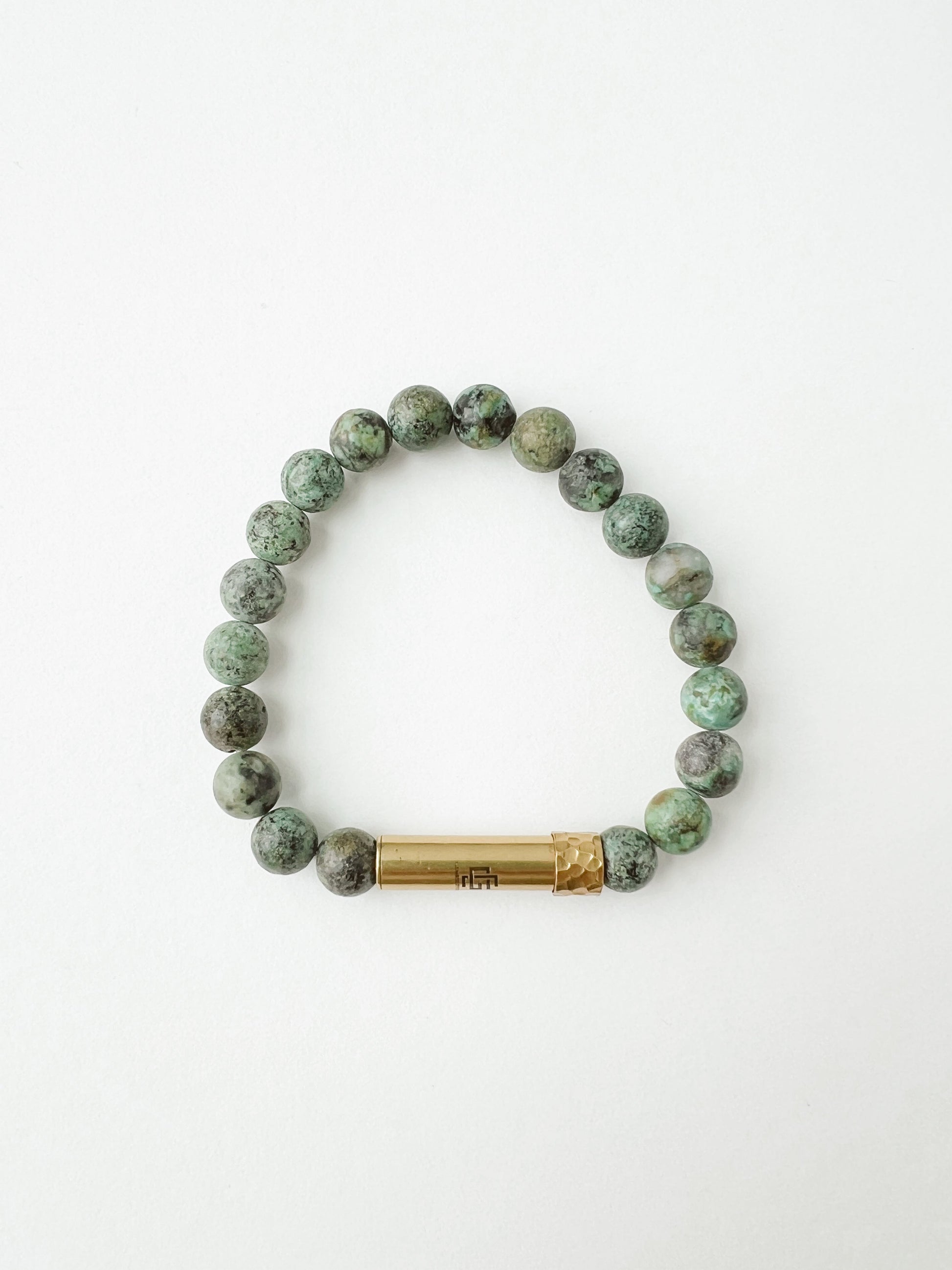 Green beaded prayer bracelet with a brass charm on a white background
