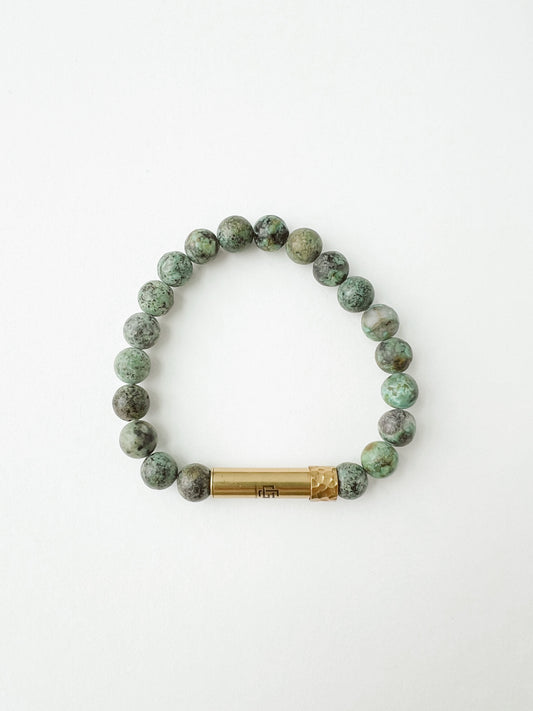 Green beaded prayer bracelet with a brass charm on a white background