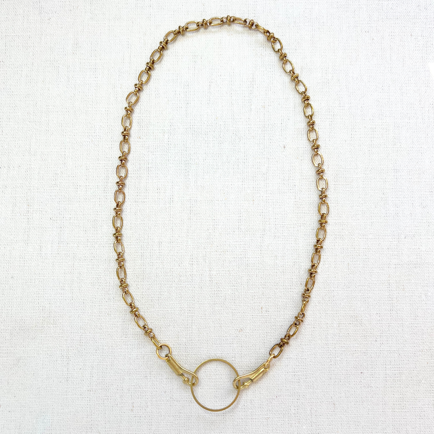 Gold chain charm necklace with a charm holder on a white fabric background