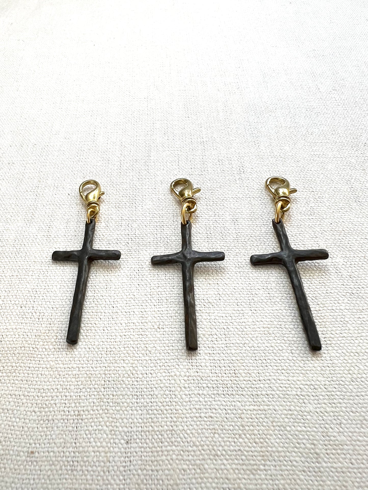 Three brown cross-shaped charms with gold clasps on a white background