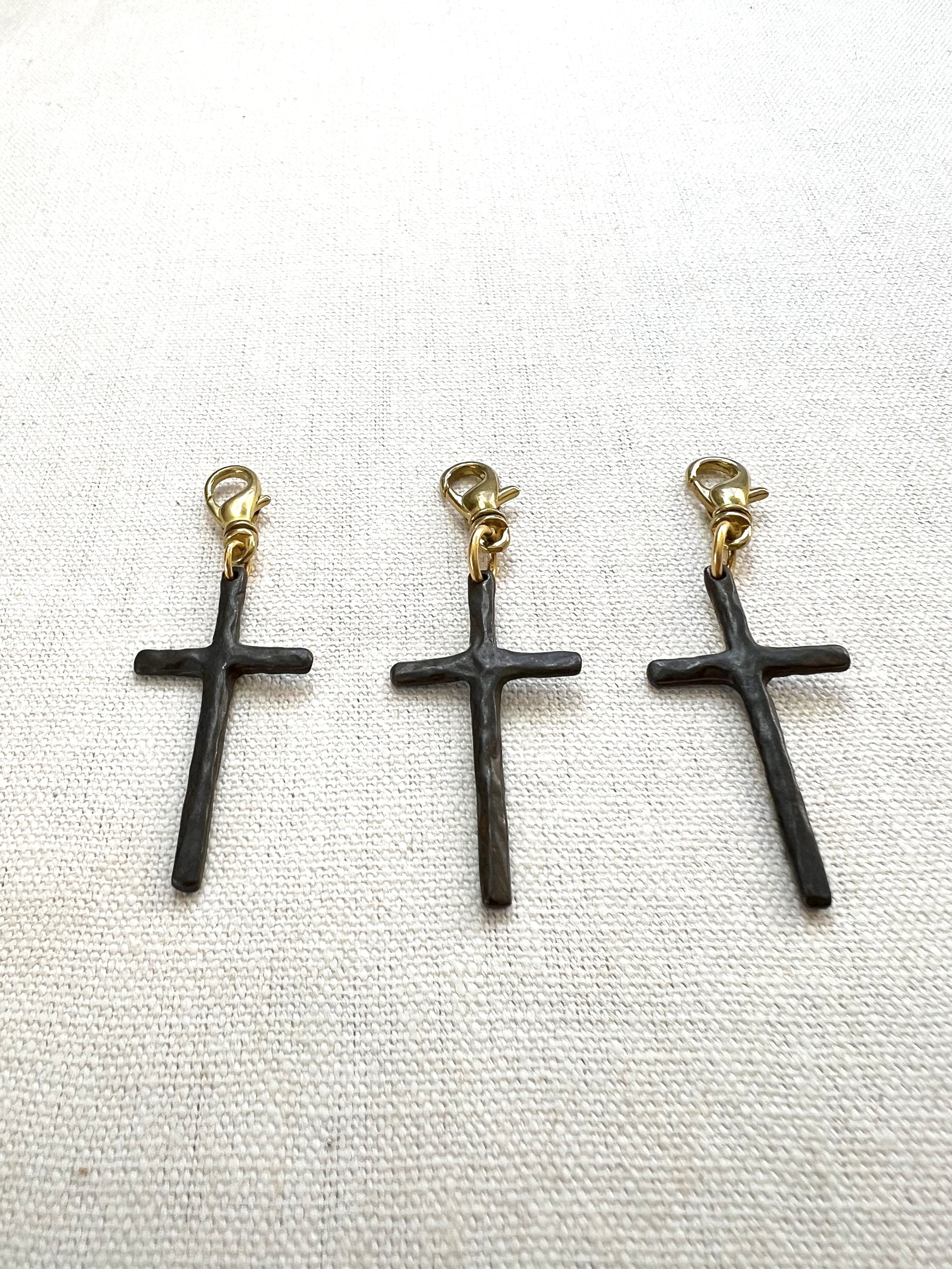 Three brown cross-shaped charms with gold clasps on a white background
